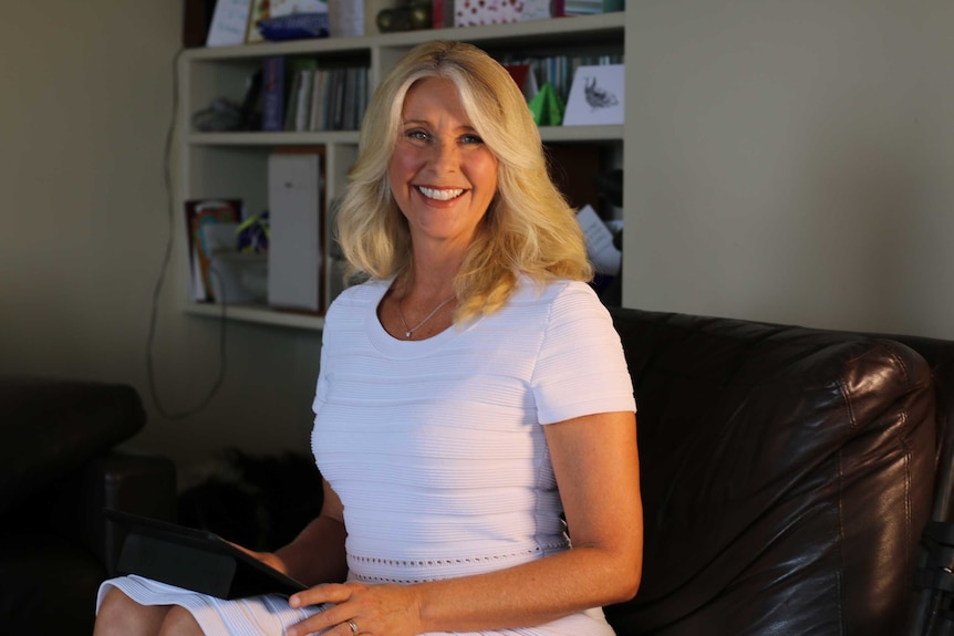 Tracey Spicer smiles on a couch in front of a bookcase