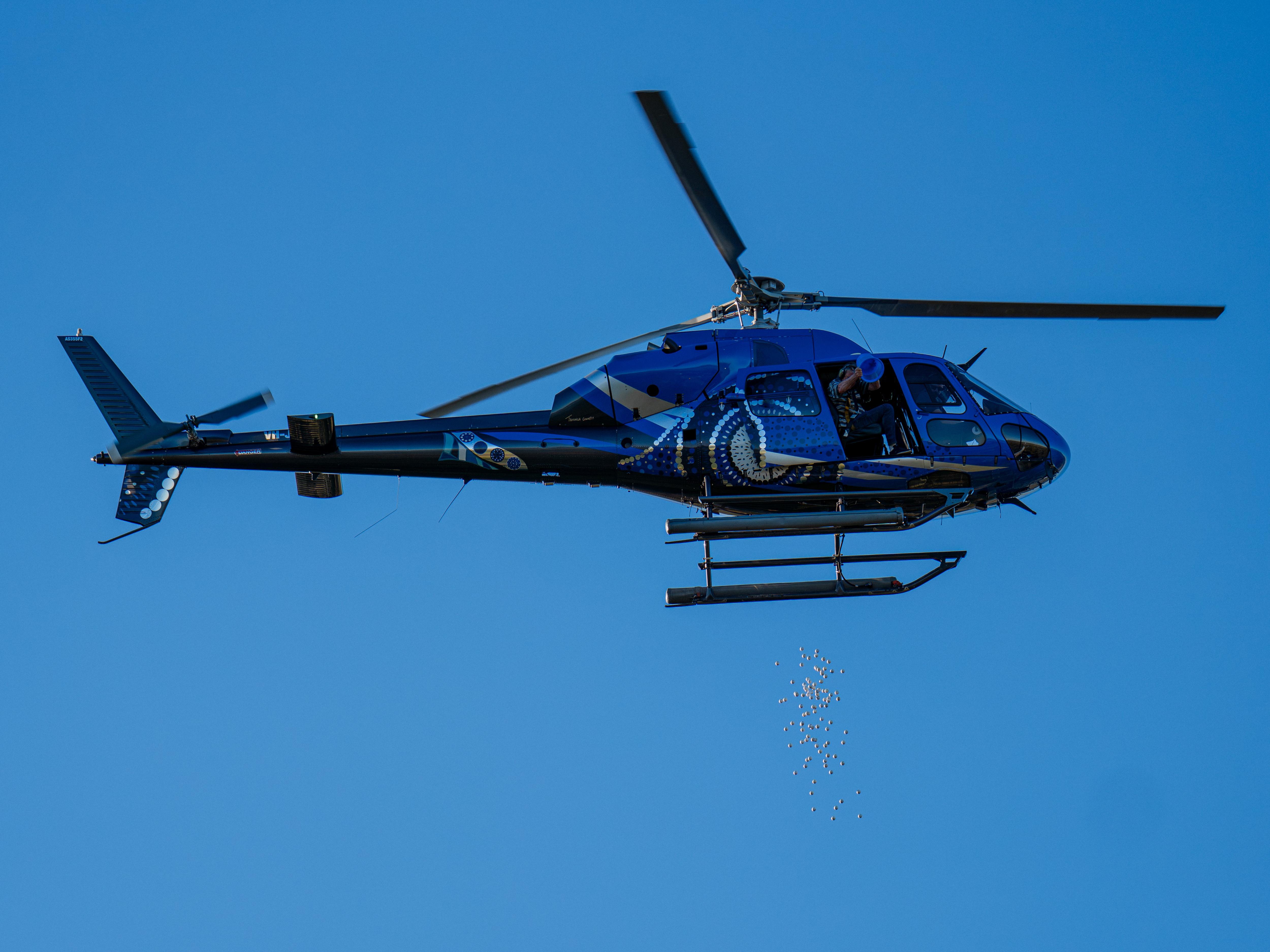dozens of golf balls fall from a blue helicopter in the sky
