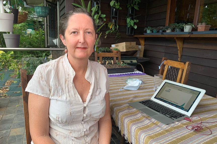 Ms Barnett wears a white, short-sleeved blouse with her hair in a pony tail and sits at an outdoor table with her laptop open.