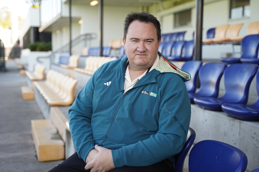 Lions Football Club manager Rob Scanlan wears a FIFA jacket while sitting in the audience grandstand