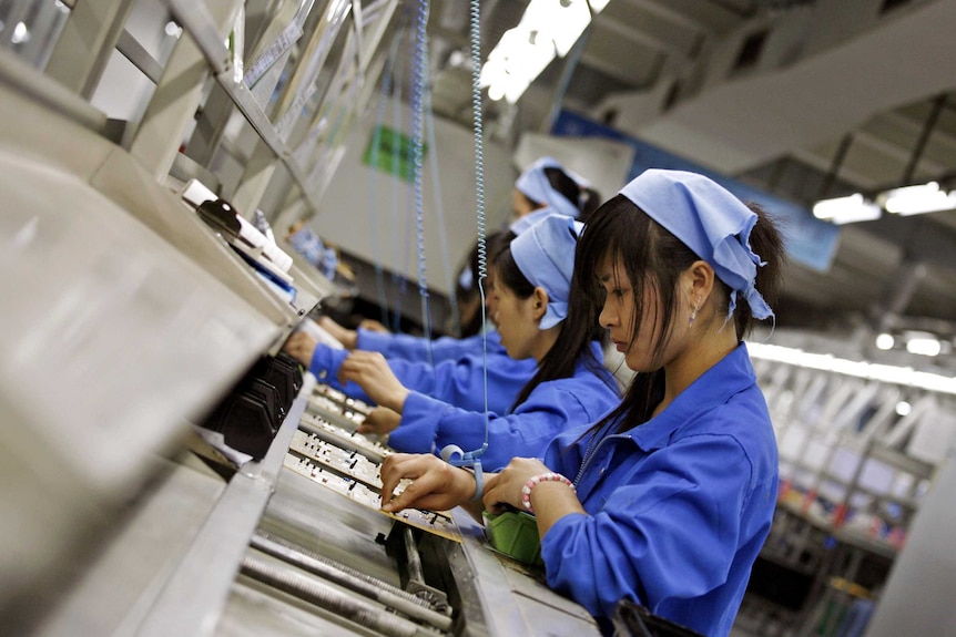 A row of female Chinese factory workers assembling electronics in a factory.