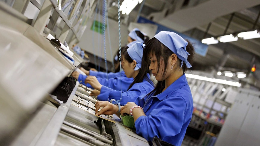 Chinese workers in blue jumpsuits place conductors on electric circuit boards in a line.