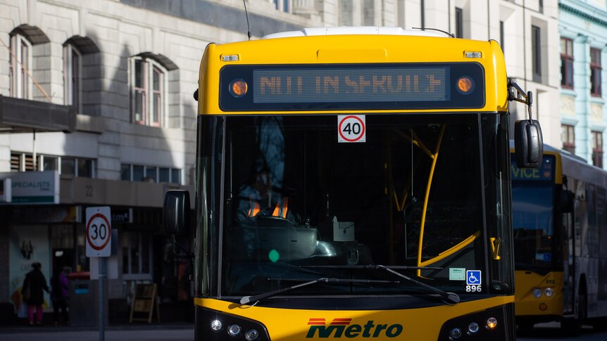 A yellow bus with a sign reading not in service in front of sandstone buildings.