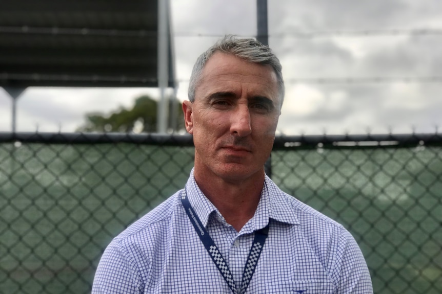 A middle-aged man with a police lanyard looks seriously at a camera