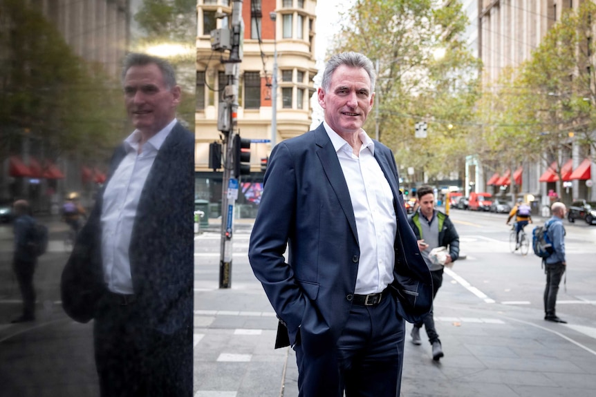 Man stands smiling in a suit on a city street