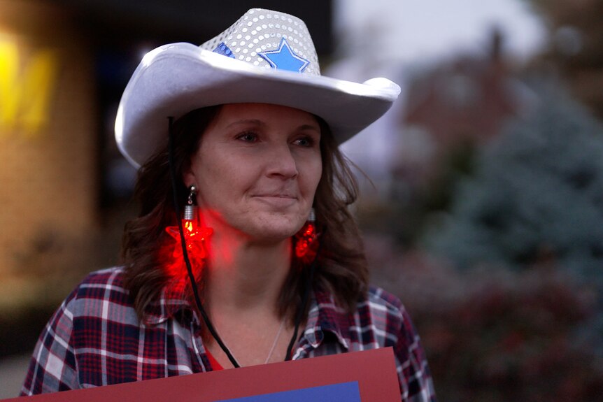 A woman wearing a silver cowboy hat with a blue star, red light-up star earrings, and a checked shirt
