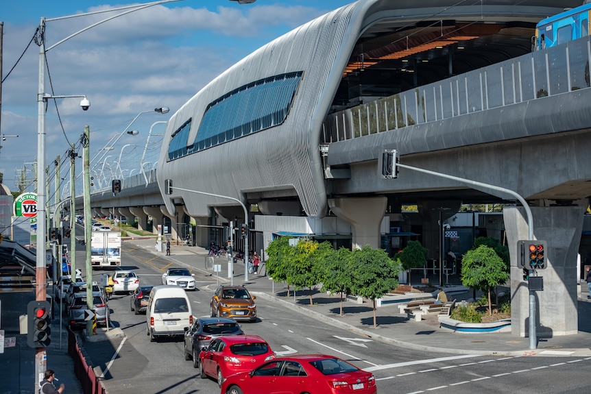 A few trees are planted near the railway line in Clayton, with car traffic at an intersection.