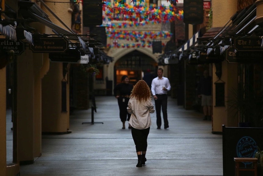 Three people walk through a deserted London Court in Perth as workers start returning to the CBD