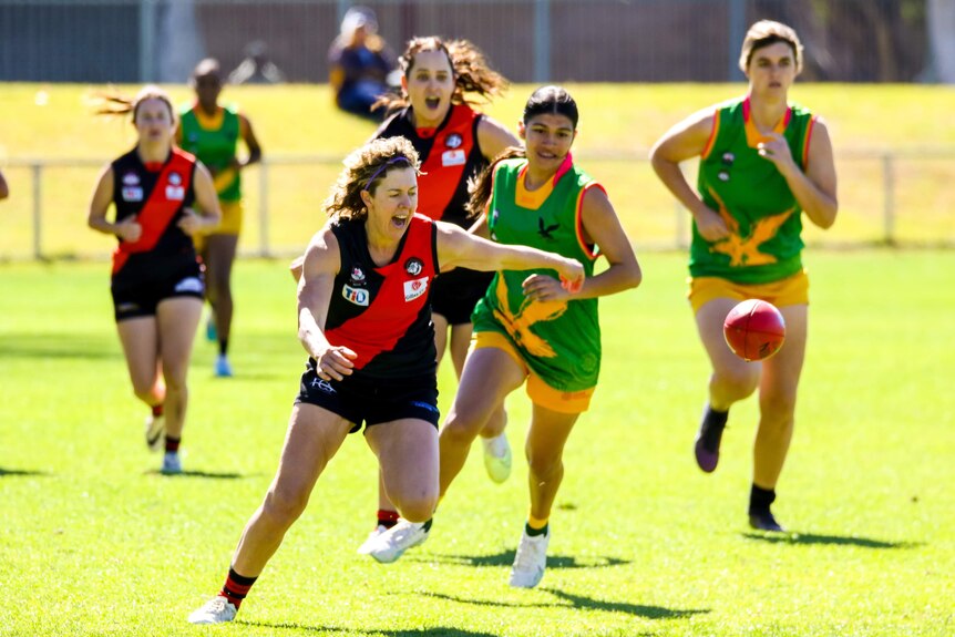 Players from two women's footy teams chase the ball.