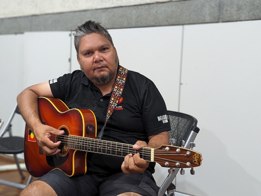 Native man in black shirt holding a guitar
