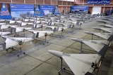 A large set of drones is pictured inside a big warehouse-like space.