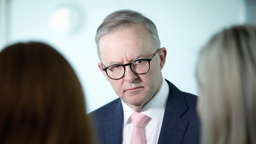 Albanese looks serious while staring at an out of focus woman, a banner behind him.