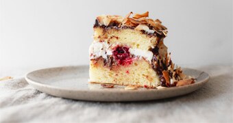 Slice of lamington cake with toasted coconut, cream, jam, fresh raspberries and chocolate ganache on a plate.