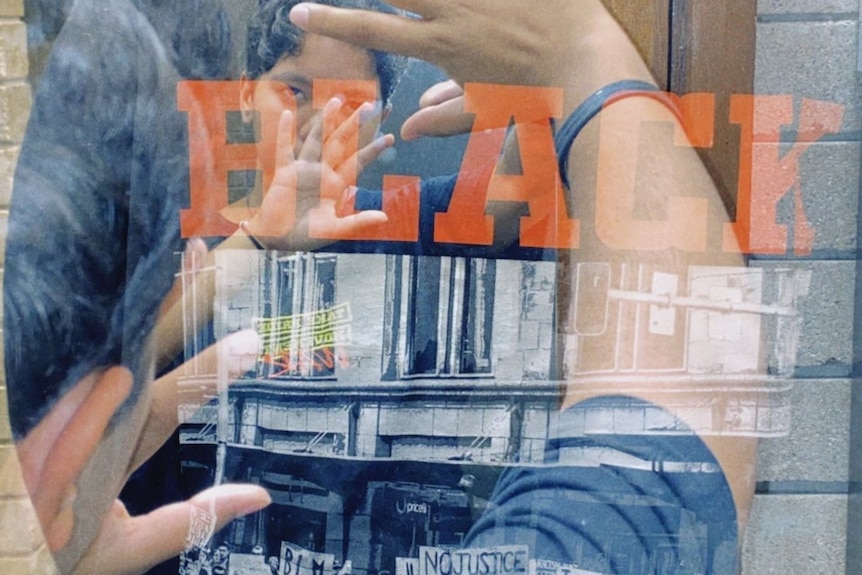 A young woman is seen in a reflection with a Black Lives Matter t-shirt held up in front of her.