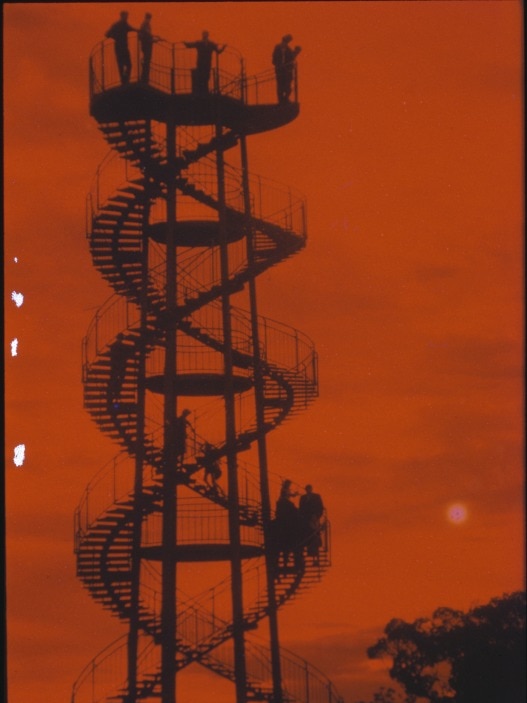 A double-spiral tower silhouetted by a red sky at dusk.