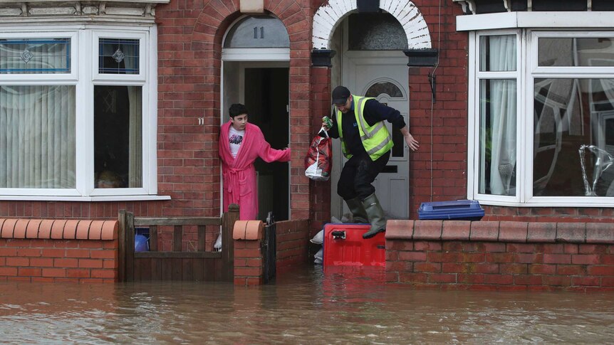 A man wearing pink nightgown leans out of his sandbagged red brick house to look at the flooded street.