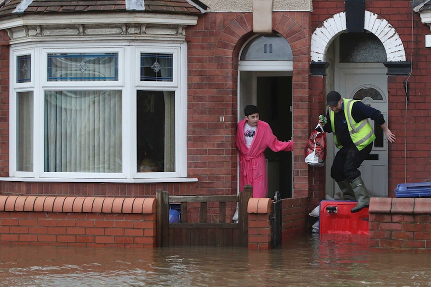 A man wearing pink nightgown leans out of his sandbagged red brick house to look at the flooded street.