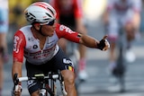 A cyclist in red white and black uniforms holds up his left index finger in celebration of a stage win.