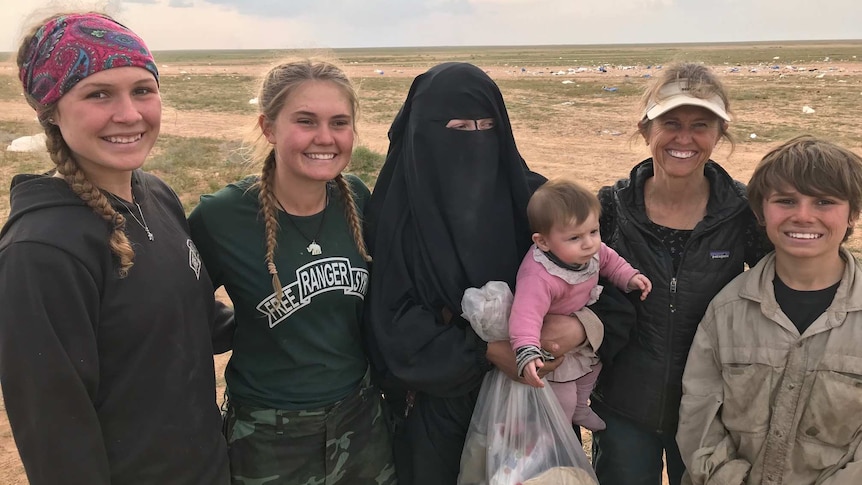 Zehra stands in a field with three women and a teenage boy. She wears a Niqab and holds a child.