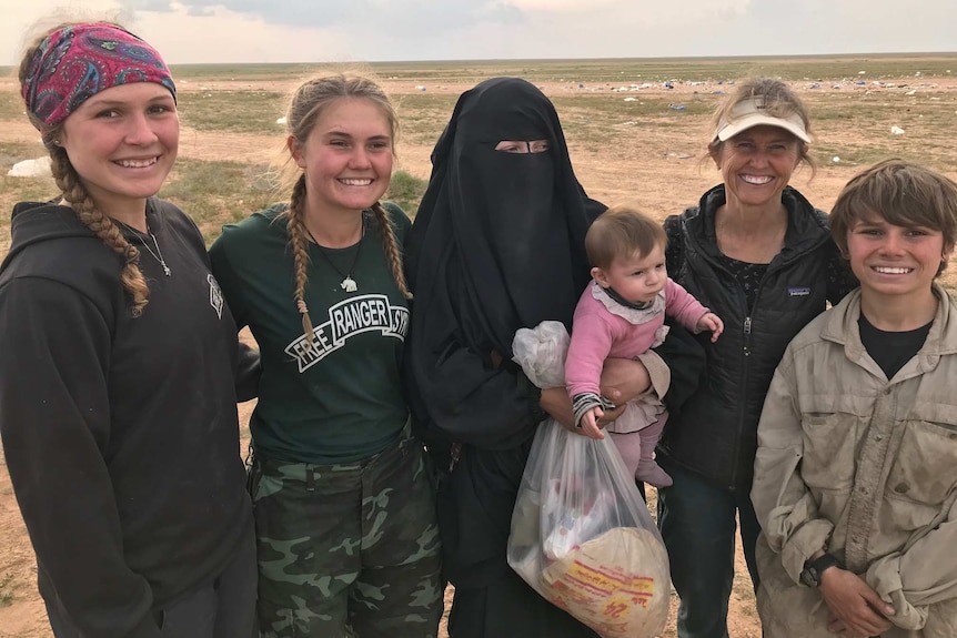 Zehra stands in a field with three women and a teenage boy. She wears a Niqab and holds a child.