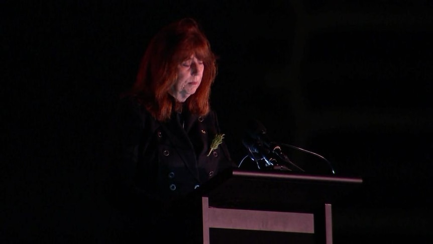 Professor Margaret Gardner, a lady with red hair standing at lectern in the dim light of dawn. 