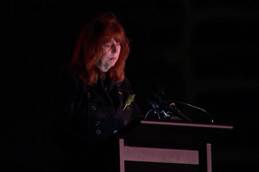 Professor Margaret Gardner, a lady with red hair standing at lectern in the dim light of dawn. 