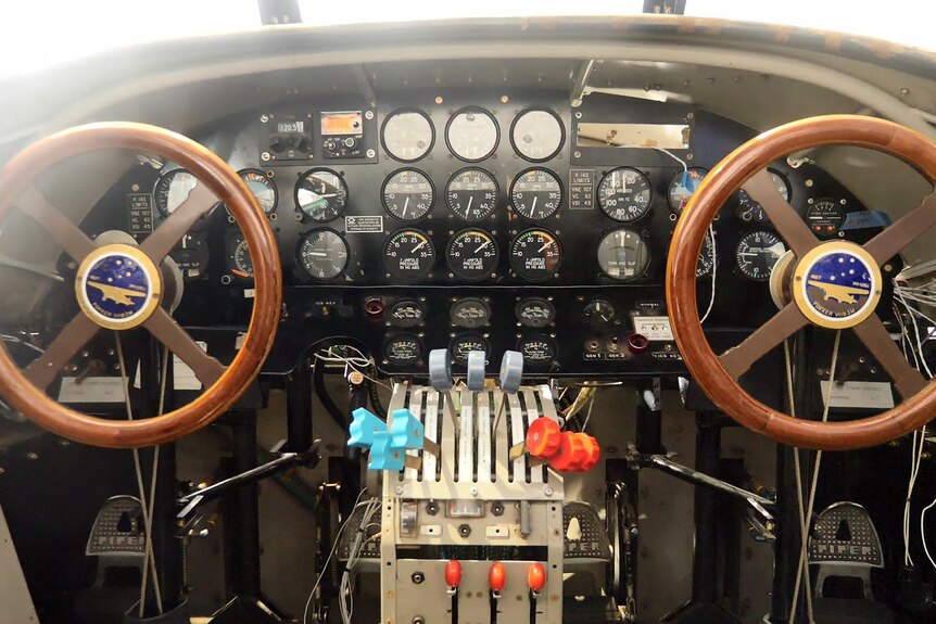 Two wooden steering wheels in front of a board of gauges and levers inside the cockpit of the Southern Cross replica.