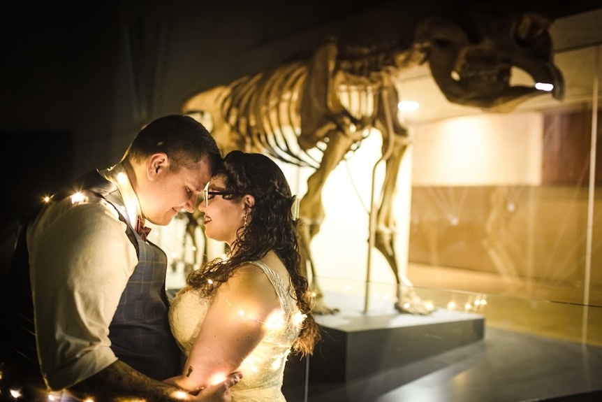 Couple dressed in wedding gown and suit infront of a dinosaur skeleton.