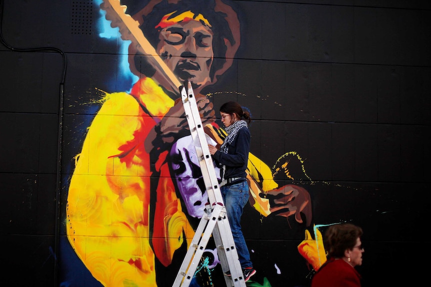 A woman paints graffiti of the rock star Jimi Hendrix, on the wall of a music shop in Malaga, southern Spain.