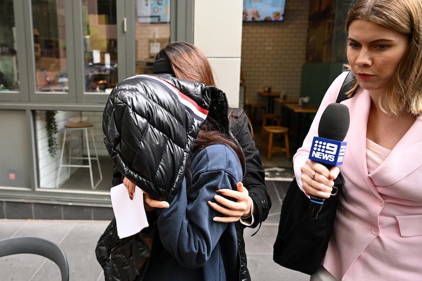 A woman leaving court with a shiny jacket over her head.