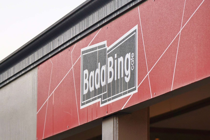 A tight angled shot of shopfront signage outside Bada Bing cafe with a black logo on a large red sign.