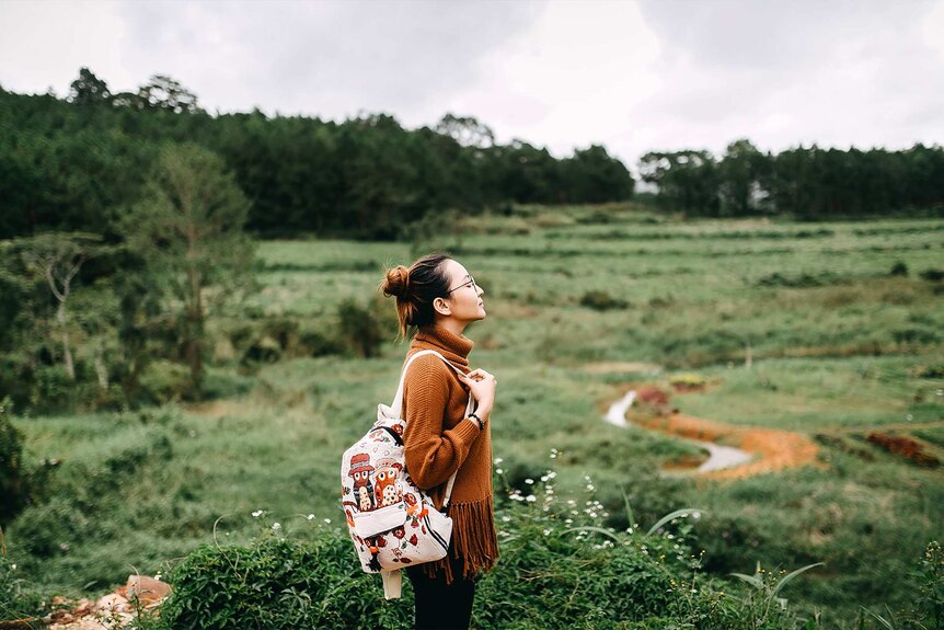 Young woman backpacker breathing in the air in an open field for a story about what travel insurance doesn't cover.
