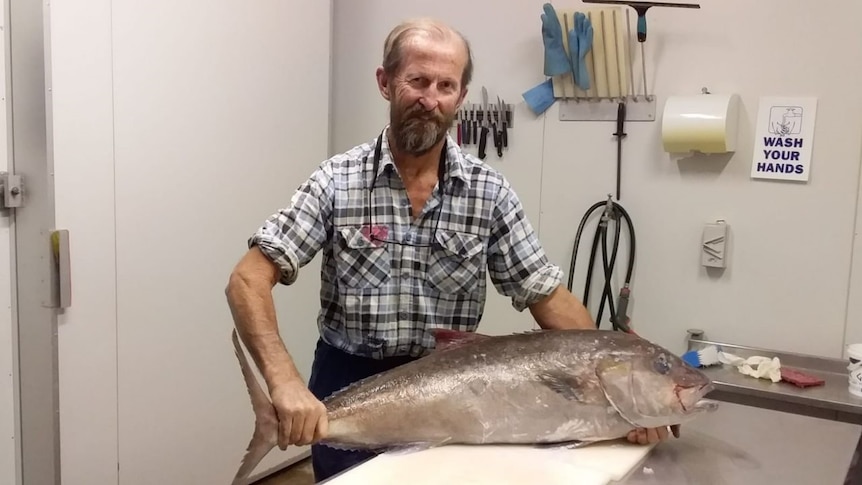 A smiling, bearded man rests his hands on a huge fish.