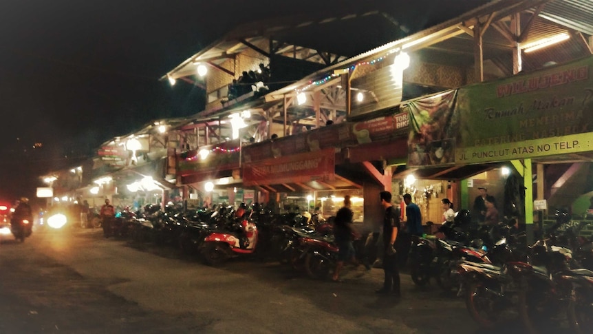 A road is filled with motorcycle parked outside a traditional restaurant in Indonesia.