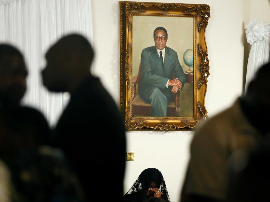 A gilded painting of Robert Mugabe in a suit looms over the top of his wife Grace whose face is covered by a mourning veil.