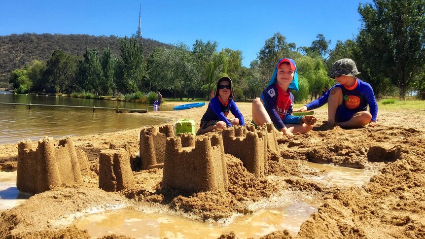 Three boys build sandcastles in Canberra.