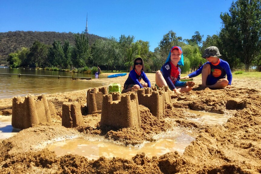 Three boys build sandcastles in Canberra.