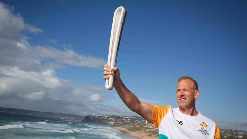 A man holds the Queen's Baton aloft with the Newcastle beach as a backdrop