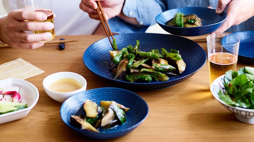 Two men serve spicy miso eggplant into smaller blue plates.