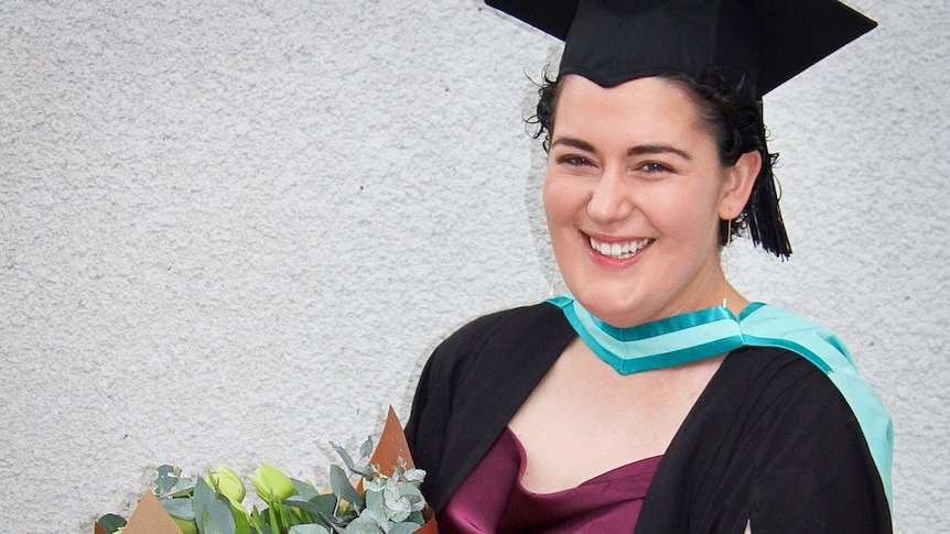 A young woman wearing university graduation gear and smiling at the camera.