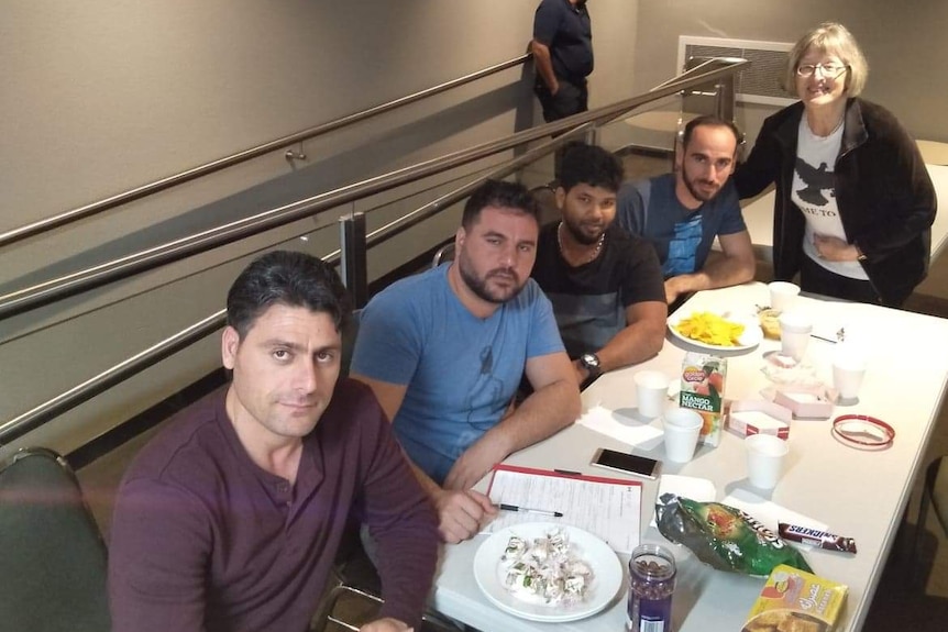 Refugee advocate Jane Salmon pictured with four men sitting around a white table with paper cups and snacks on it.