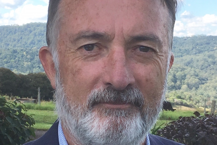 Outdoor countryside headshot of Dr Peter Simmons wearing a suit jacket and shirt