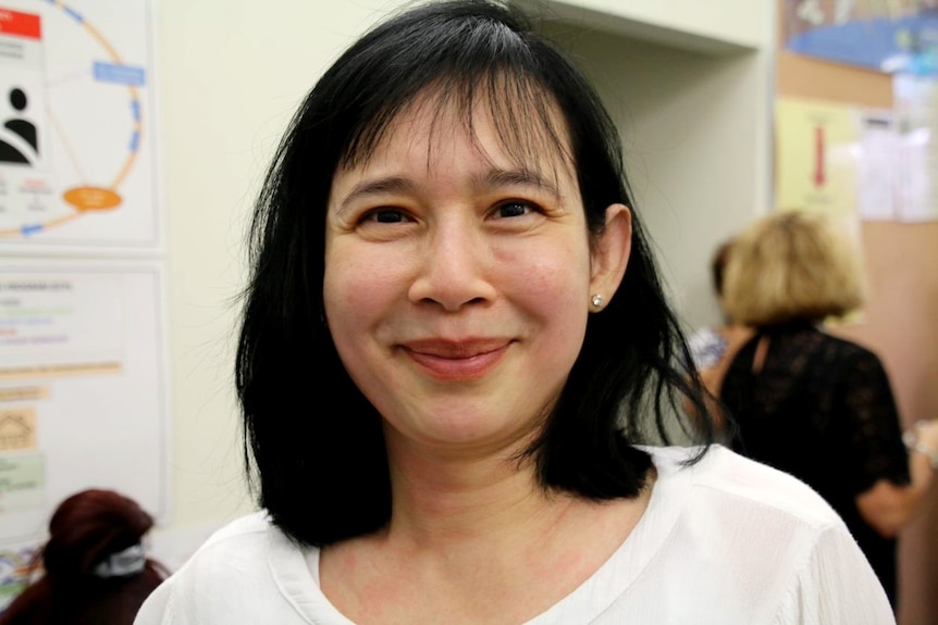 A close up of a woman wearing a white t-shirt with another woman in the background.