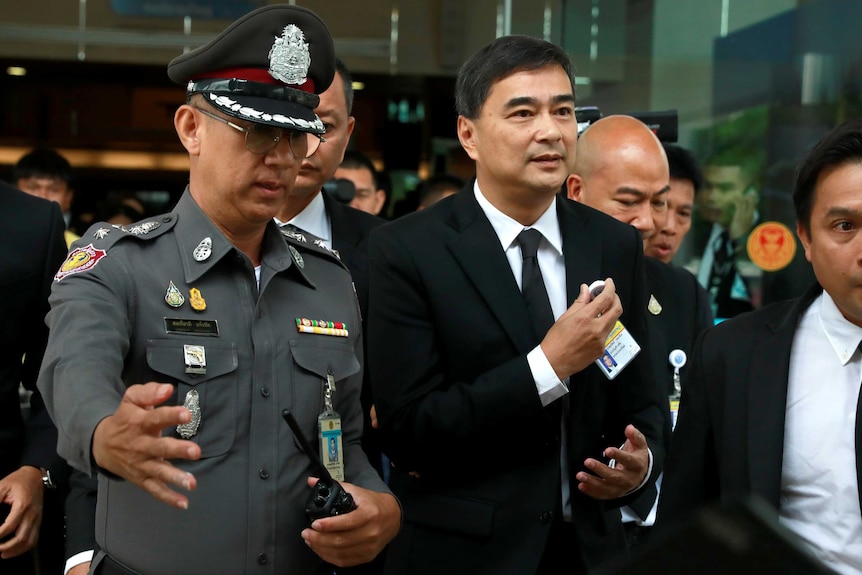 A man in a suit is escorted by a police officer.