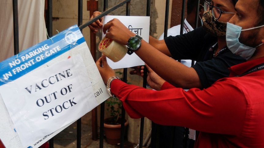 A masked man and woman tape signs to a fence saying "Vaccine out of stock".