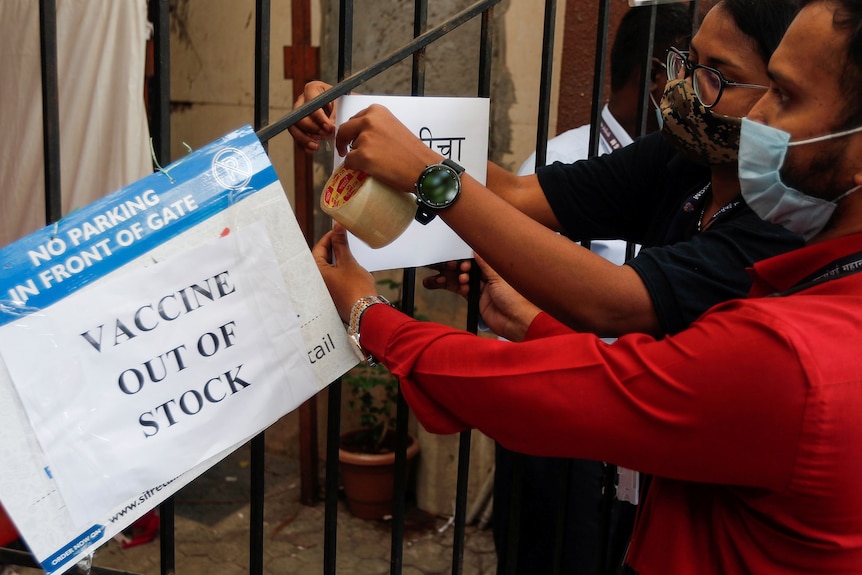 Un bărbat și o femeie, mascați, semnează gardul, spun "Vaccinul nu este disponibil".