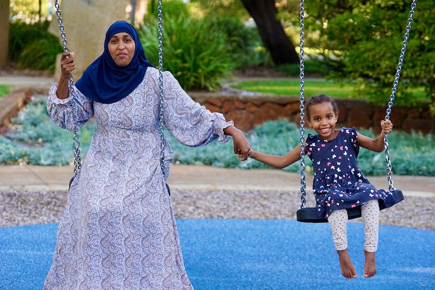A woman on the swings with her young daughter.