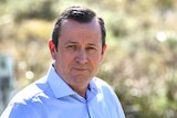 Mark McGowan smiles as he stands with his hands on his hips, wearing a light blue shirt