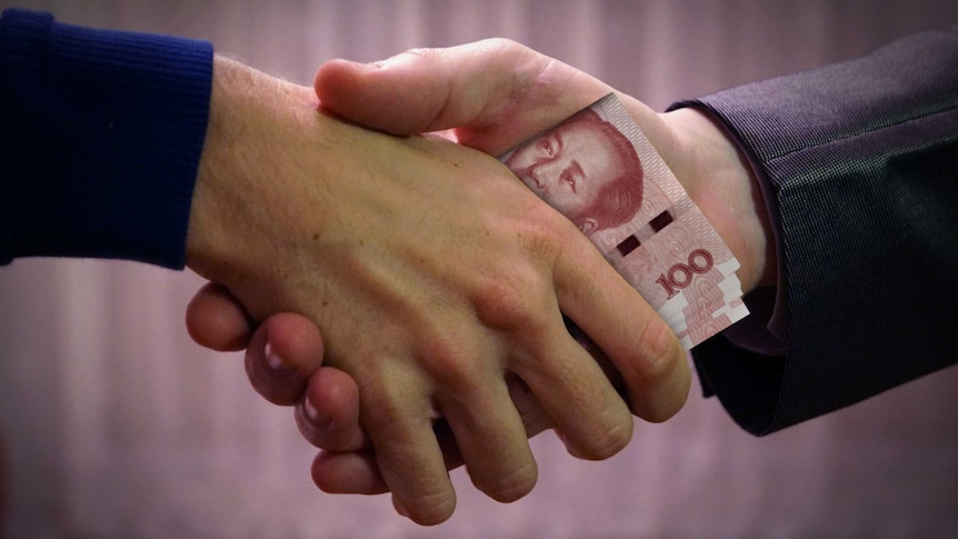 Two men shake hands while clutching Chinese 100 yuan notes.