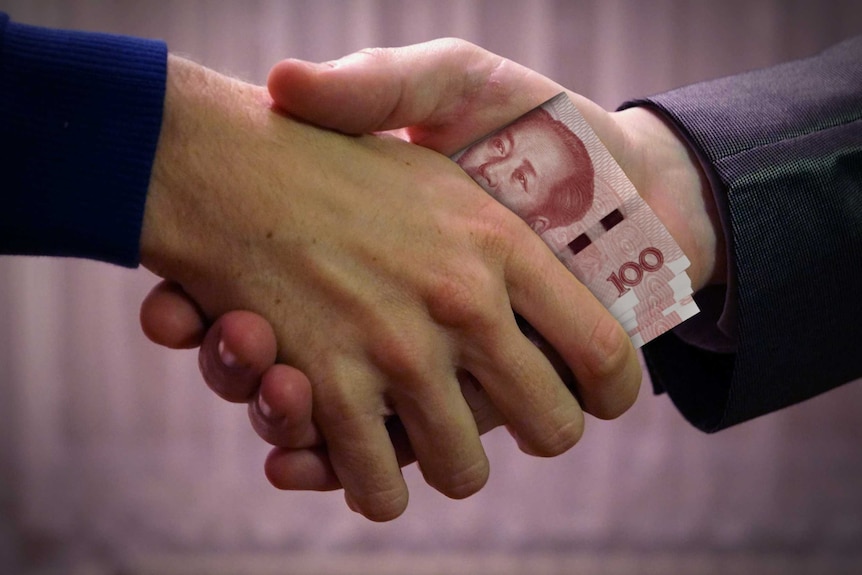 Two men shake hands while clutching Chinese 100 yuan notes.